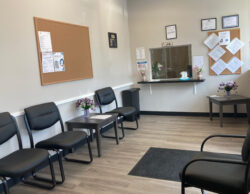 Gray room with black chairs along the left wall, bulletin board above the chairs and reception desk in the middle against the back wall