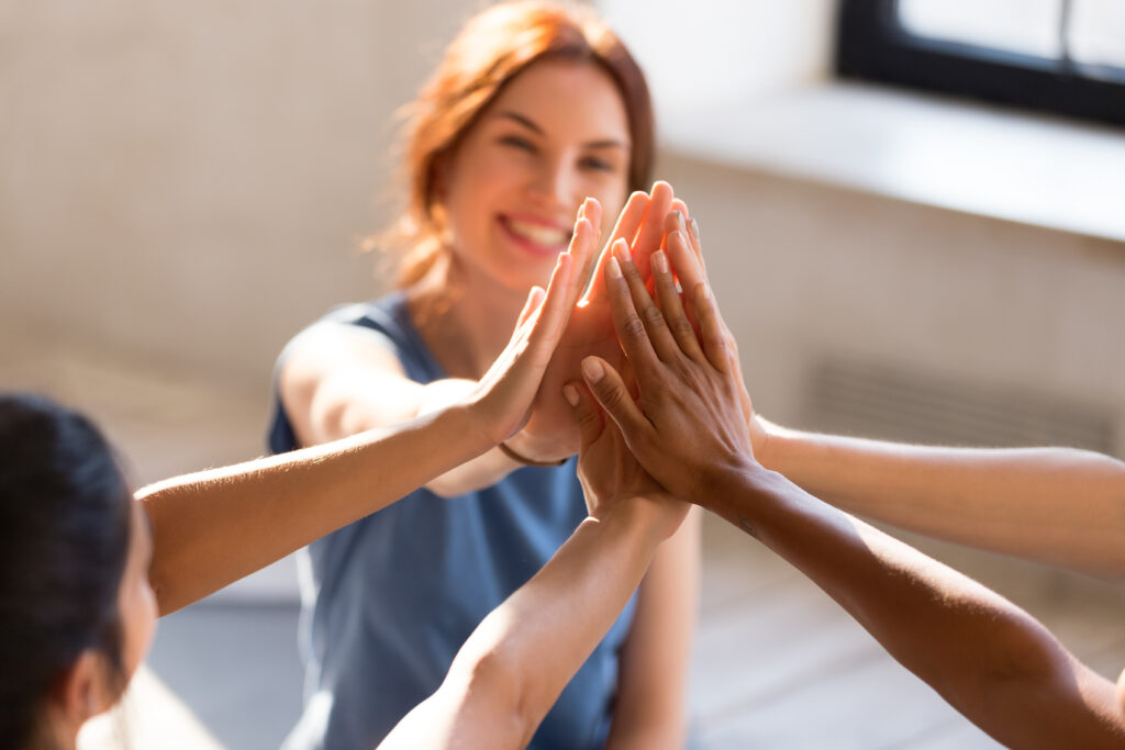 Cheerful diverse young girls sitting together in sports studio before starts training giving high five feel happy and healthy, close up focus on hands. Respect and trust, celebration and amity concept