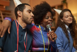 Multiethnic group of adult friends singing to microphone and enjoying karaoke during home party