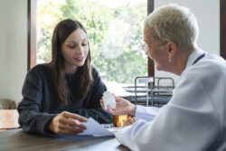 Elderly female doctor in white coat talking with beautiful young patient in clinic, giving advice on heart disease treatment and health care and medicine, medicine concept.