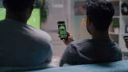 Indian men placing stakes on smartphones and speaking while sitting on sofa and watching soccer match together